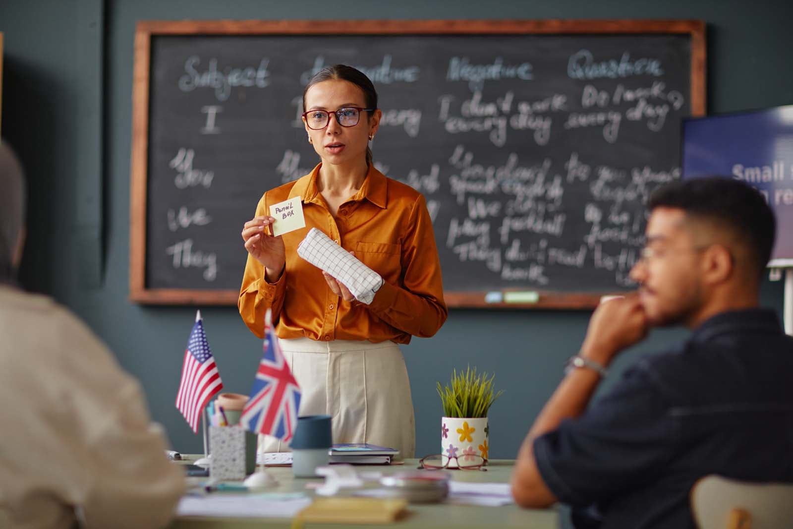 A teacher introducing vocabulary at a chalkboard while students follow along.